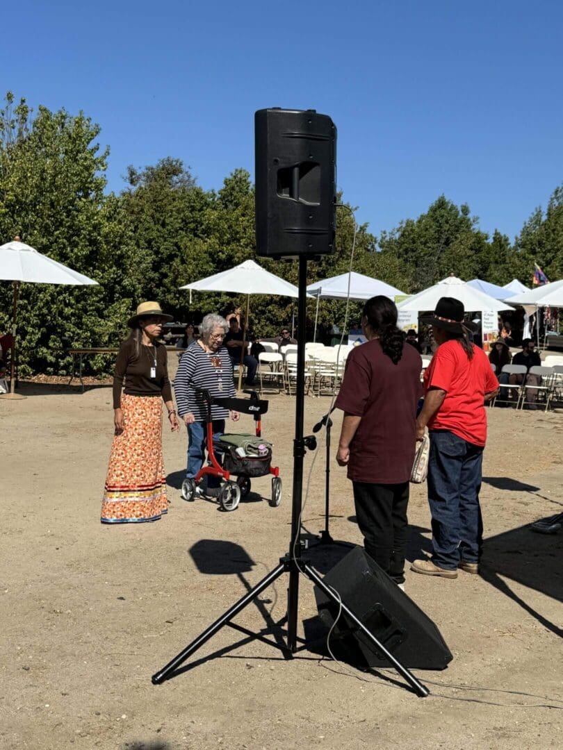 Group of people gathered outdoors near a speaker and tents.