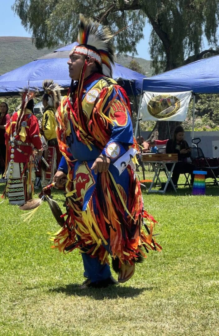 Native American dancers in colorful traditional regalia at an outdoor event.