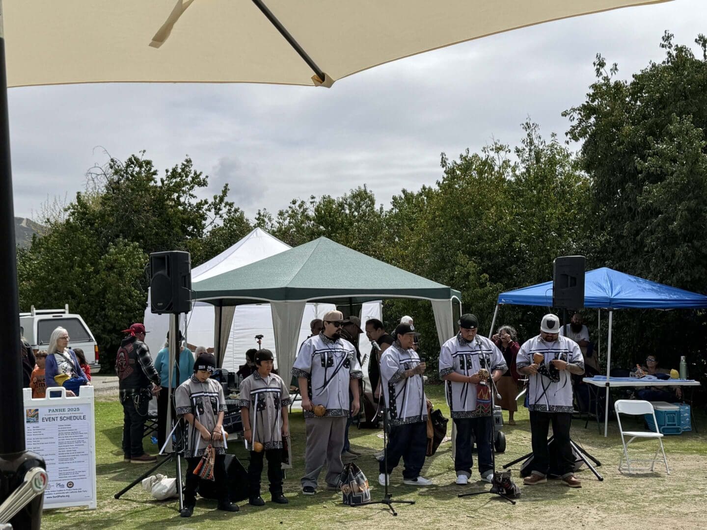 Group of people gathered outdoors under umbrellas and tents.