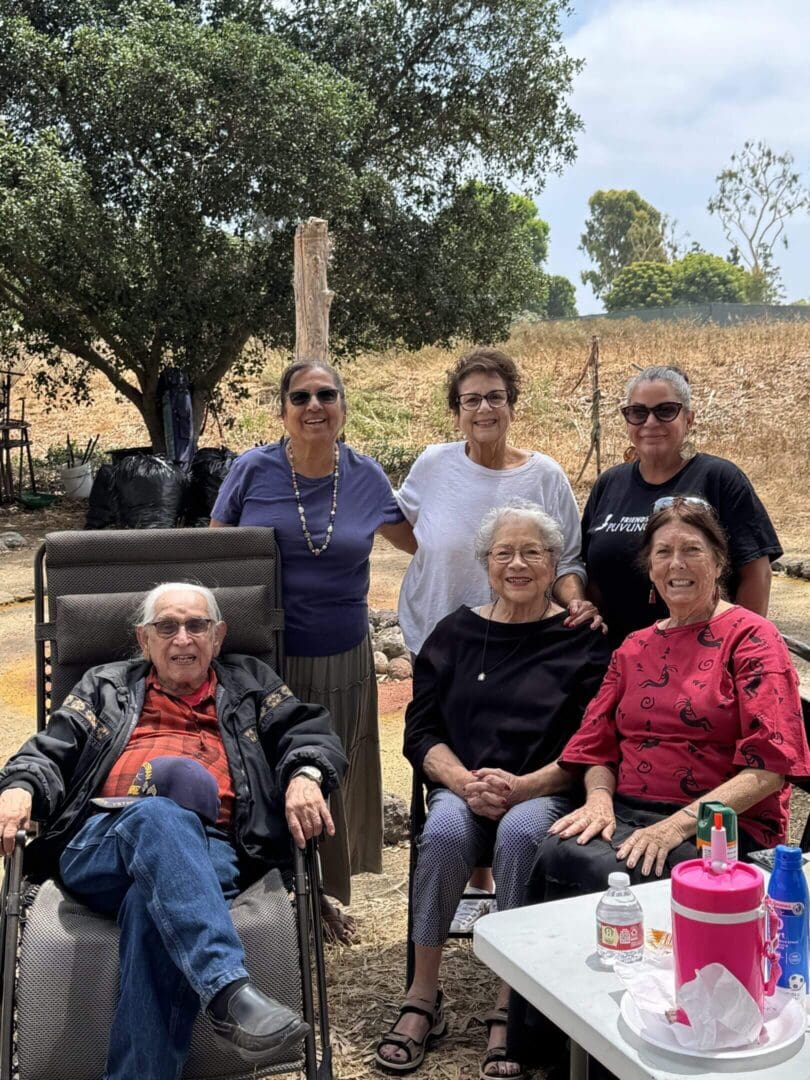 A group of six older adults posing outdoors on a sunny day.