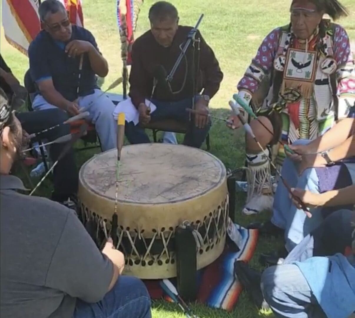 Group playing a large traditional drum outdoors.