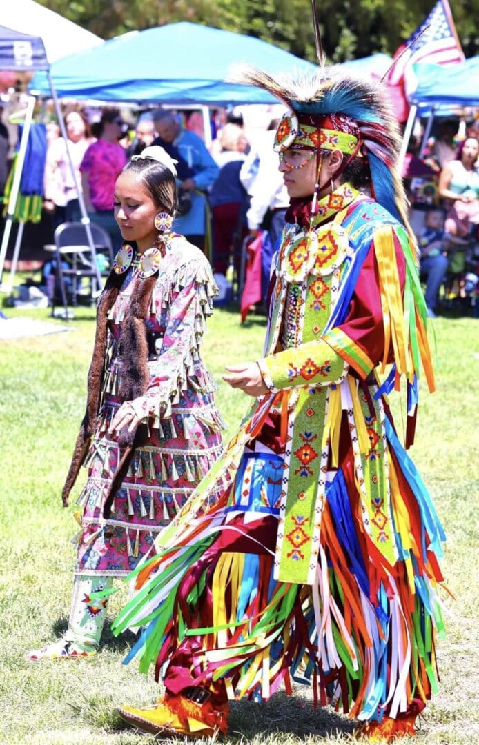Two people in colorful traditional Native American regalia at a cultural event.