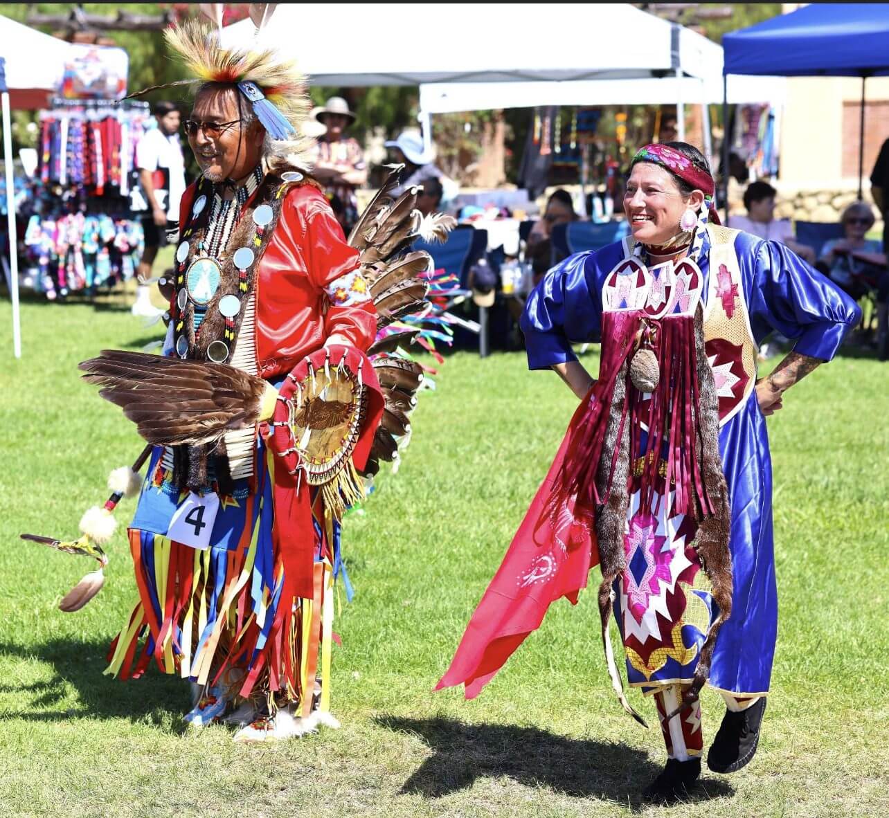 Dancers in vibrant traditional Native American regalia perform outdoors.