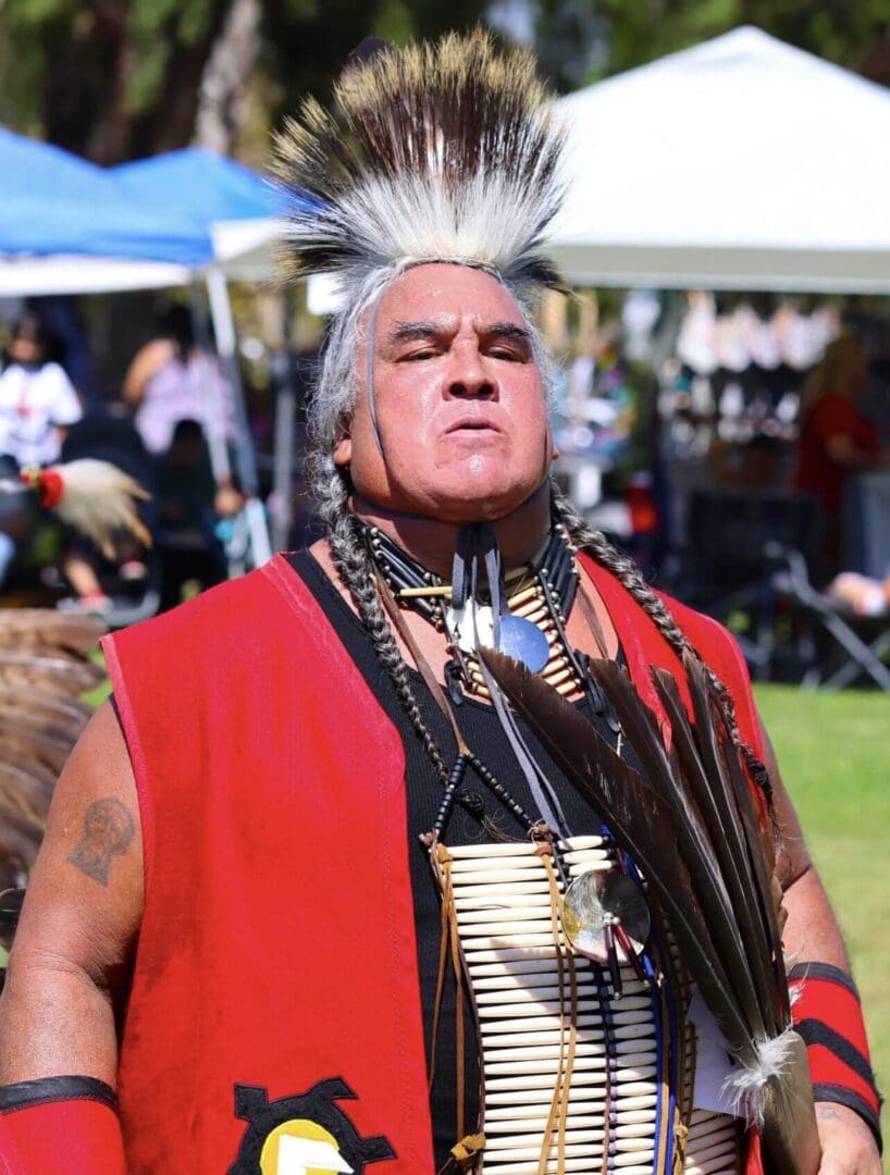 A man in traditional Native American attire at an outdoor event.