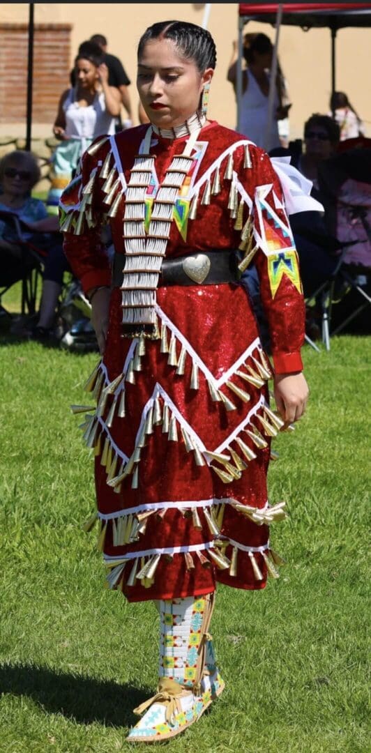 Person in a detailed red Native American regalia with white fringe and beadwork.