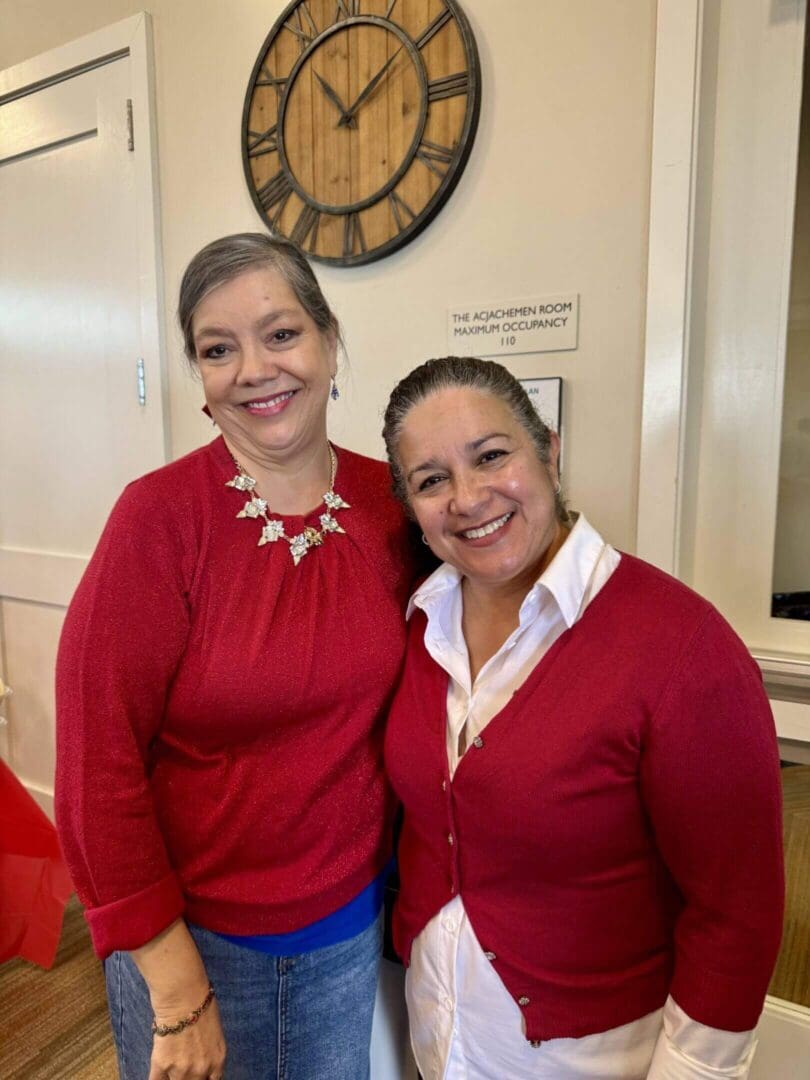 Two women smiling indoors near clock.