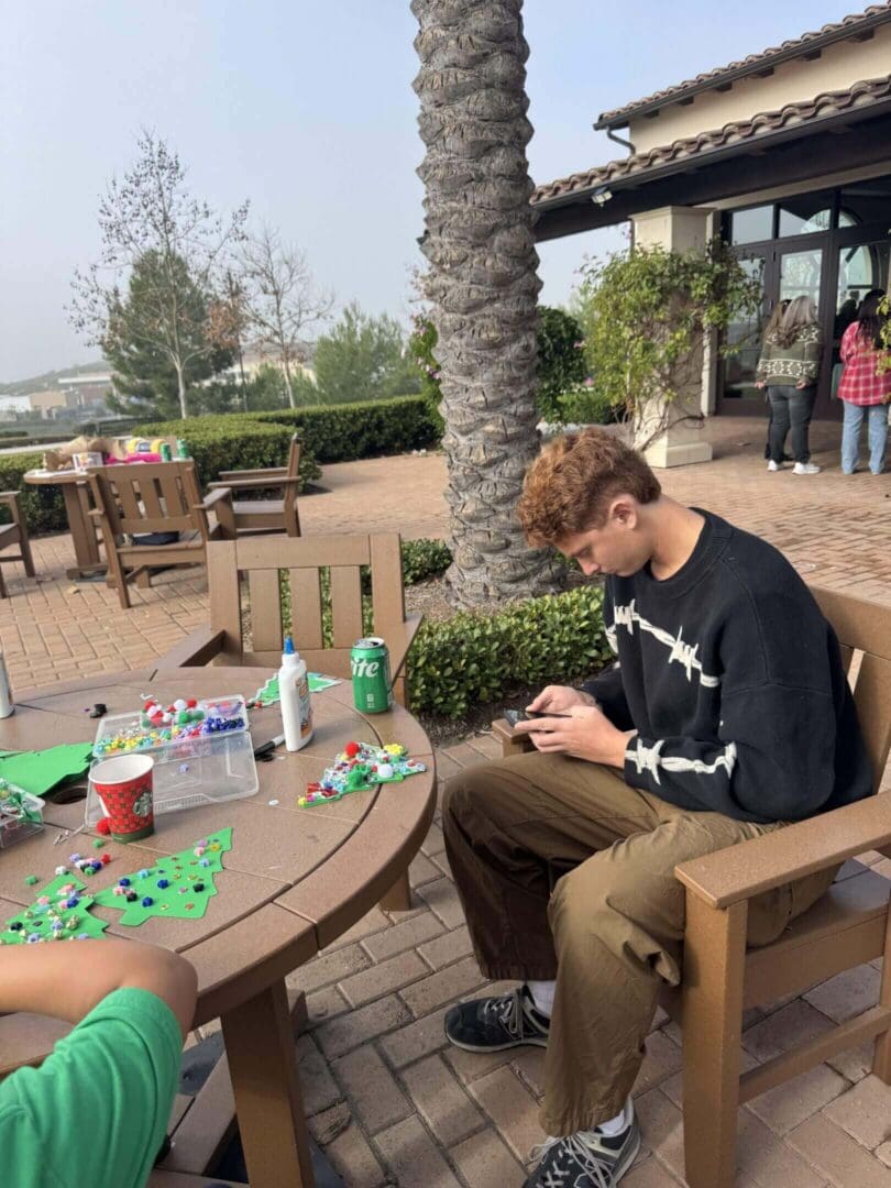 Person crafting at outdoor table, using phone.
