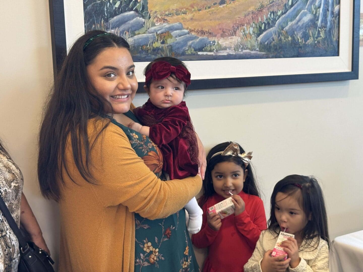 Smiling woman holding baby, two children nearby.