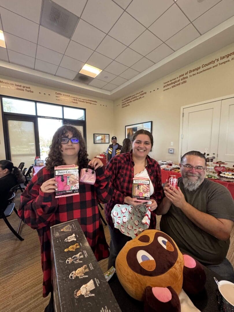 Three people holding gifts, smiling indoors.
