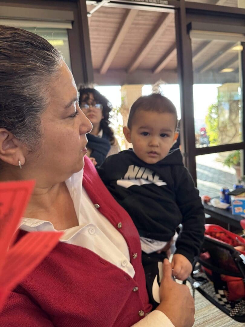 Woman holding a child indoors, window background.