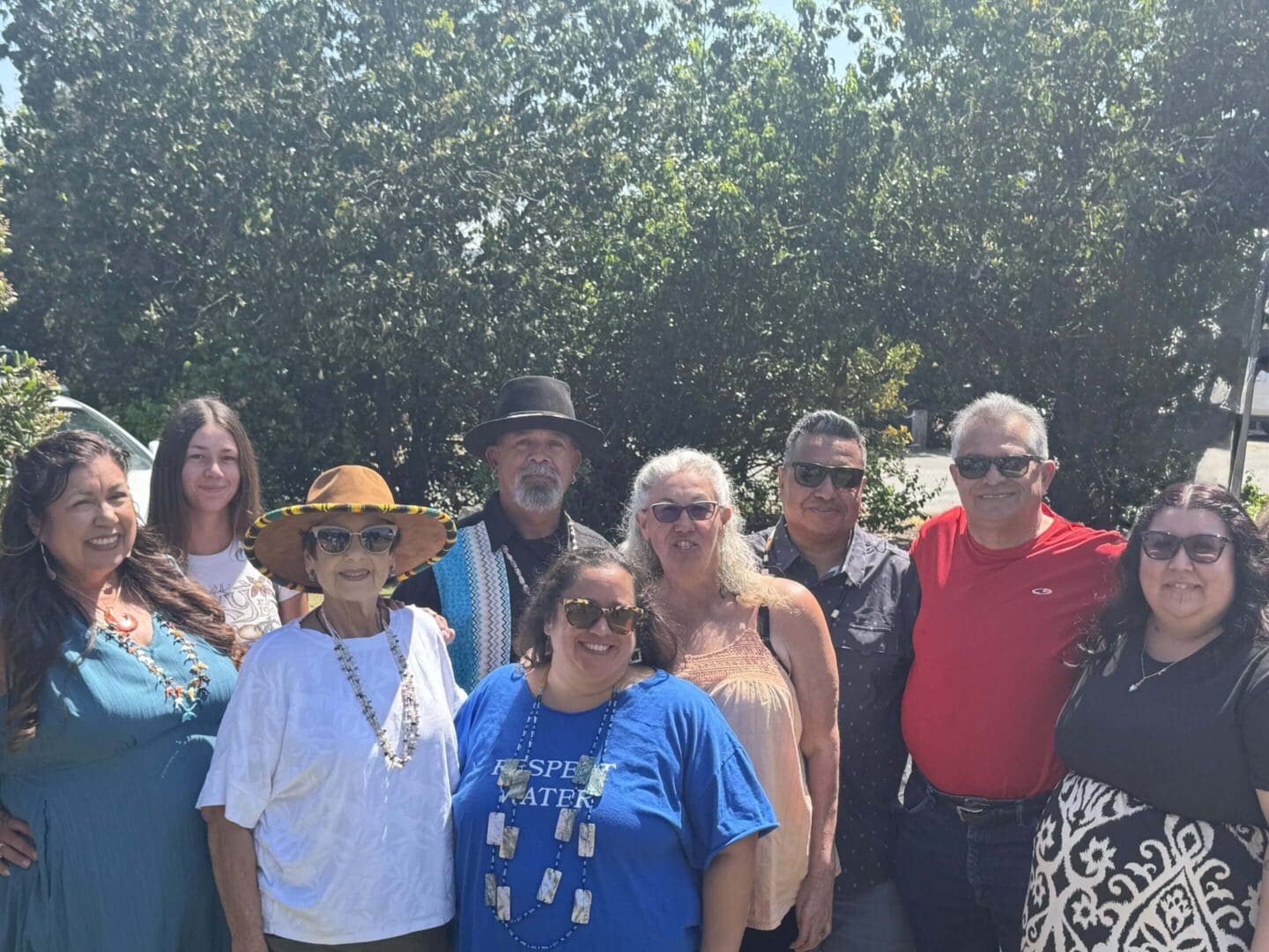Group of people smiling outdoors under trees.